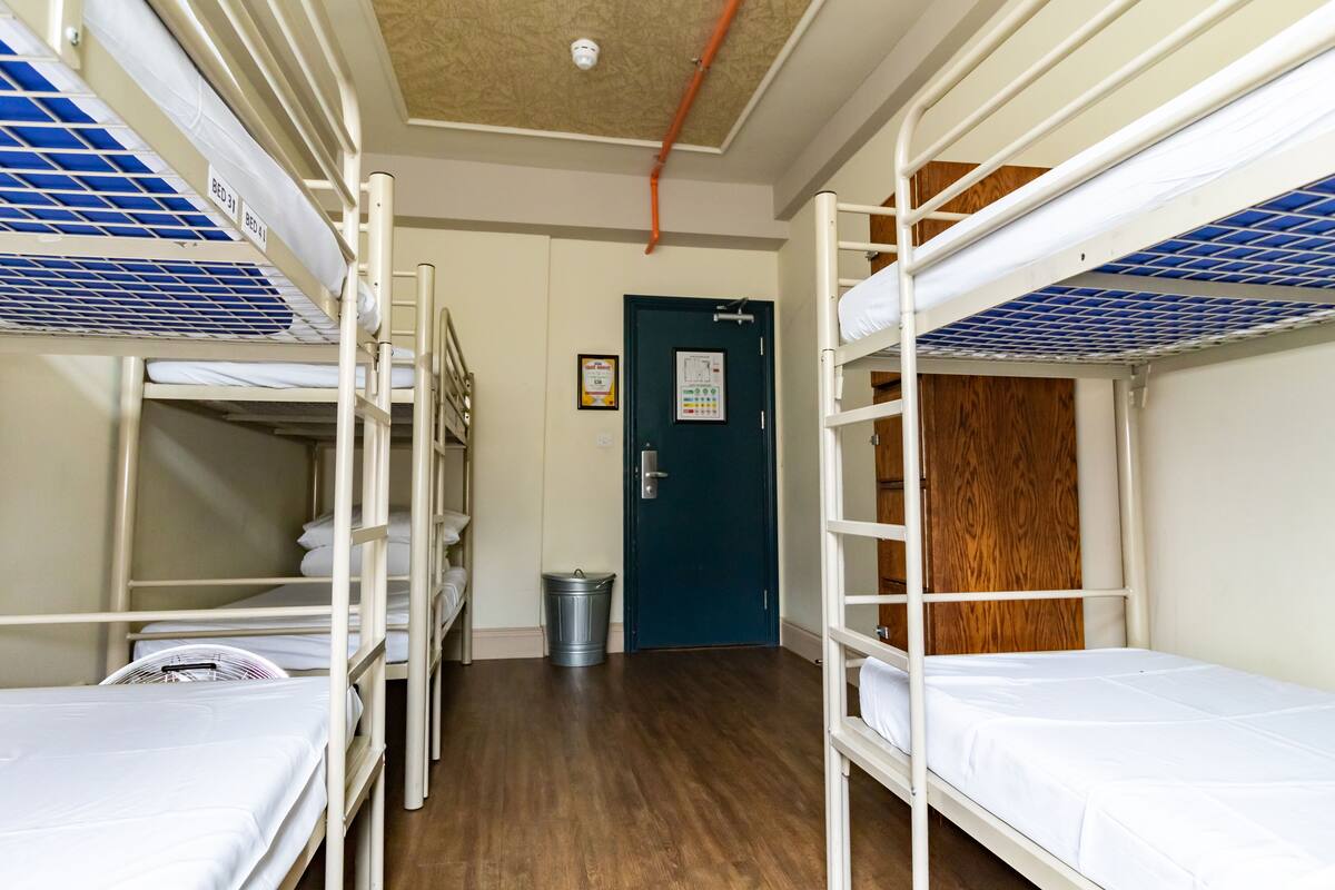 Ein Schlafsaalzimmer mit Etagenbetten, einer Holztür und einem Mülleimer.