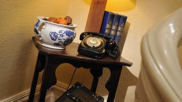 A small table with a lamp, a bowl of fruit, a vintage telephone, and a suitcase.