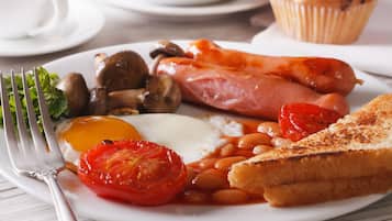 A plate of breakfast food including eggs, tomatoes, beans, mushrooms, sausages, and toast.