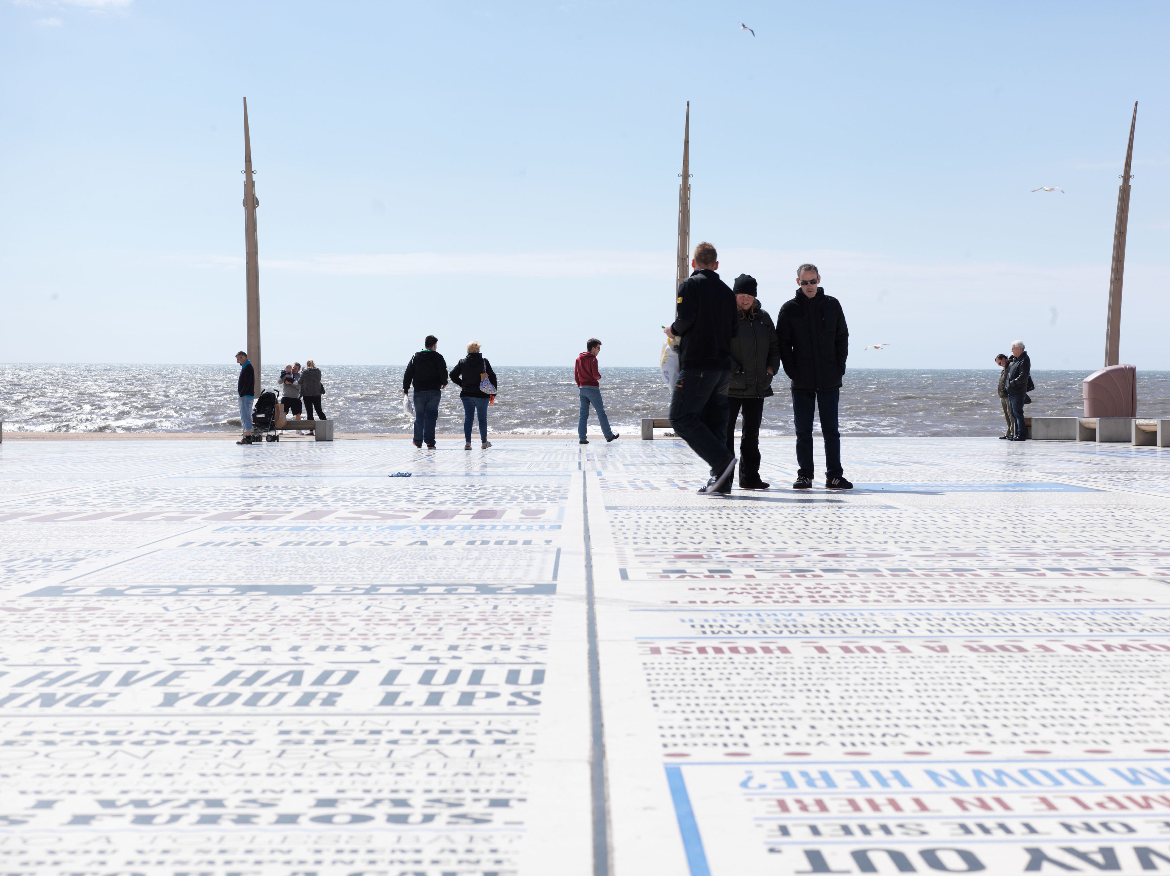 A tiled walkway with people walking, overlooking a body of water.