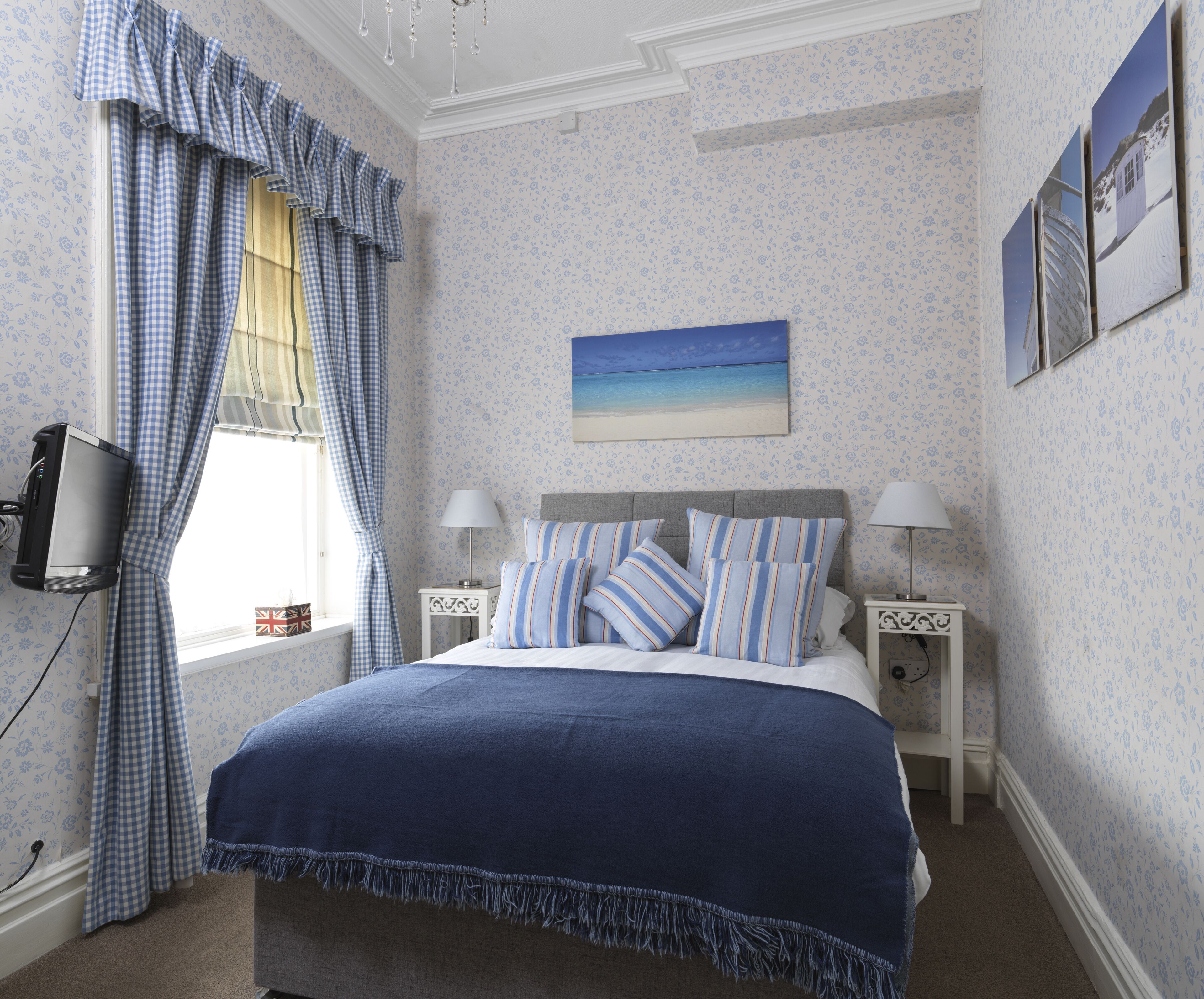 A bedroom with a bed, two bedside tables, a television, and a window with curtains.