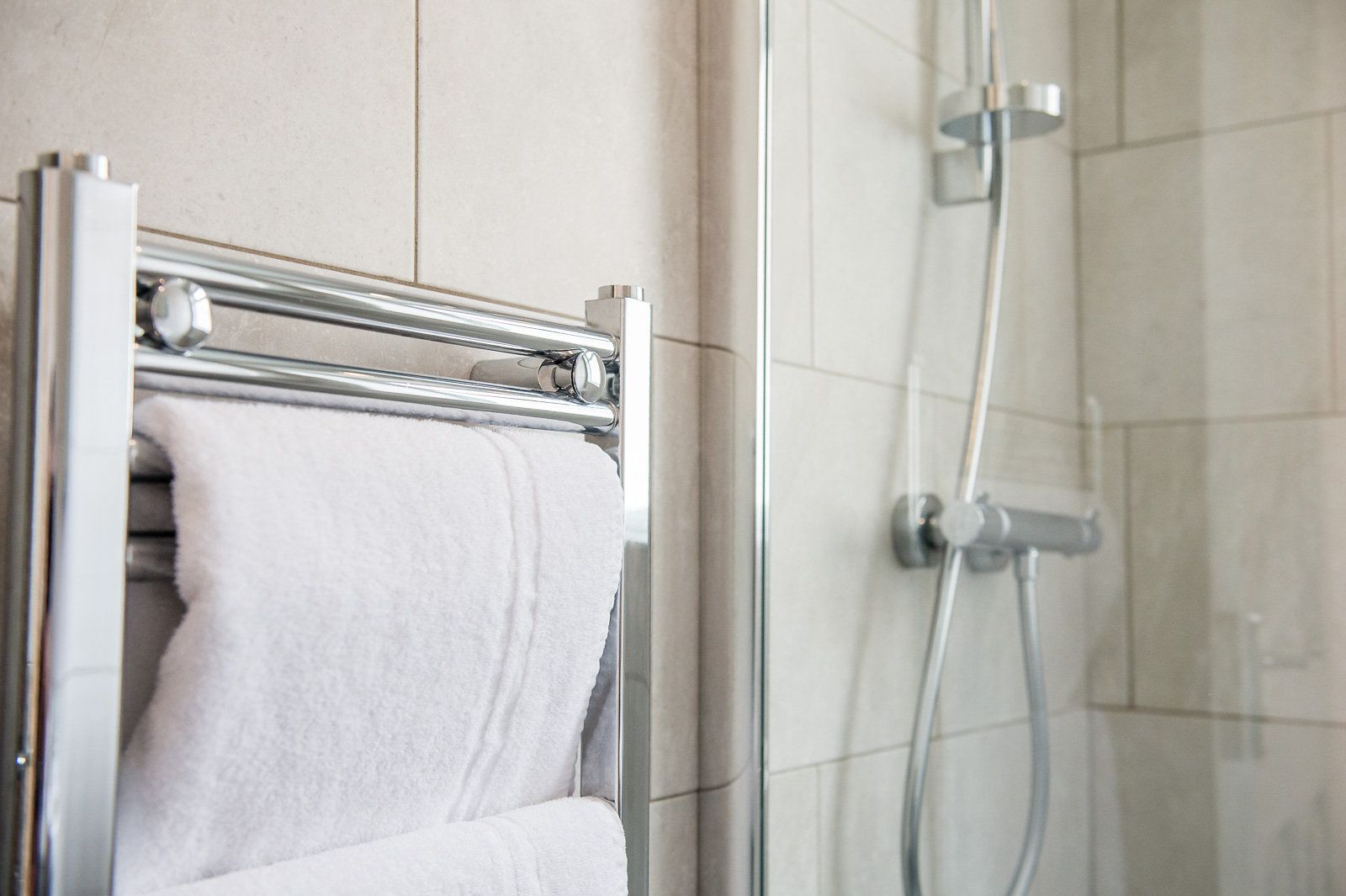 Un baño con mampara de vidrio, toallero cromado y una toalla blanca, además de un cabezal de ducha instalado en la pared.