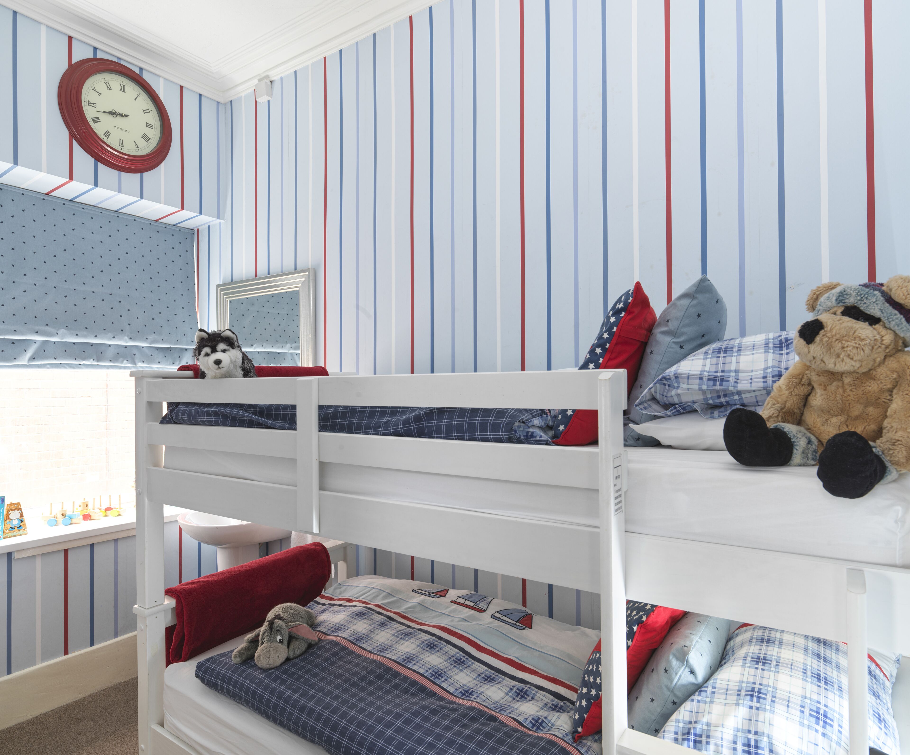 A child's bunk bed with a window, a clock, and a teddy bear.