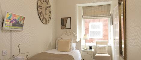 A bedroom with a bed, bedside table, lamp, and a clock on the wall.