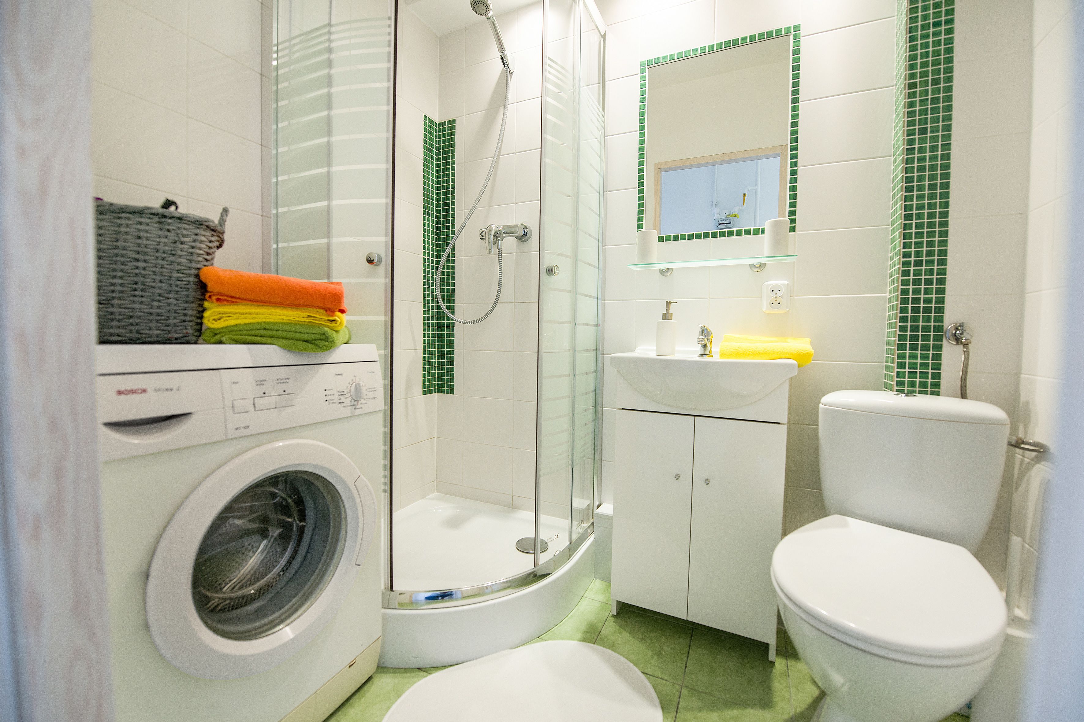 Un baño pequeño con lavadora, cabina de ducha de vidrio, inodoro y lavamanos.