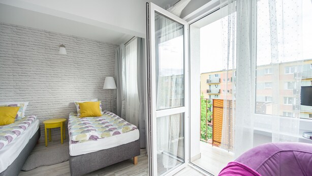 A modern bedroom with two beds, a small table, and a large window with a view of buildings. - Fresh Apart (Bydgoszcz)