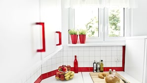 A kitchen with white cabinets, a red backsplash, a window with plants, and a cutting board with bread and a knife. - Fresh Apart (Bydgoszcz)