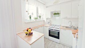 A modern kitchen with white cabinets, a wooden countertop, a gas stove, and a sink. - Fresh Apart (Bydgoszcz)