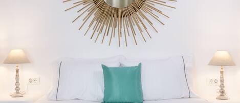 A bed with white bedding, a teal pillow, and a patterned throw.
