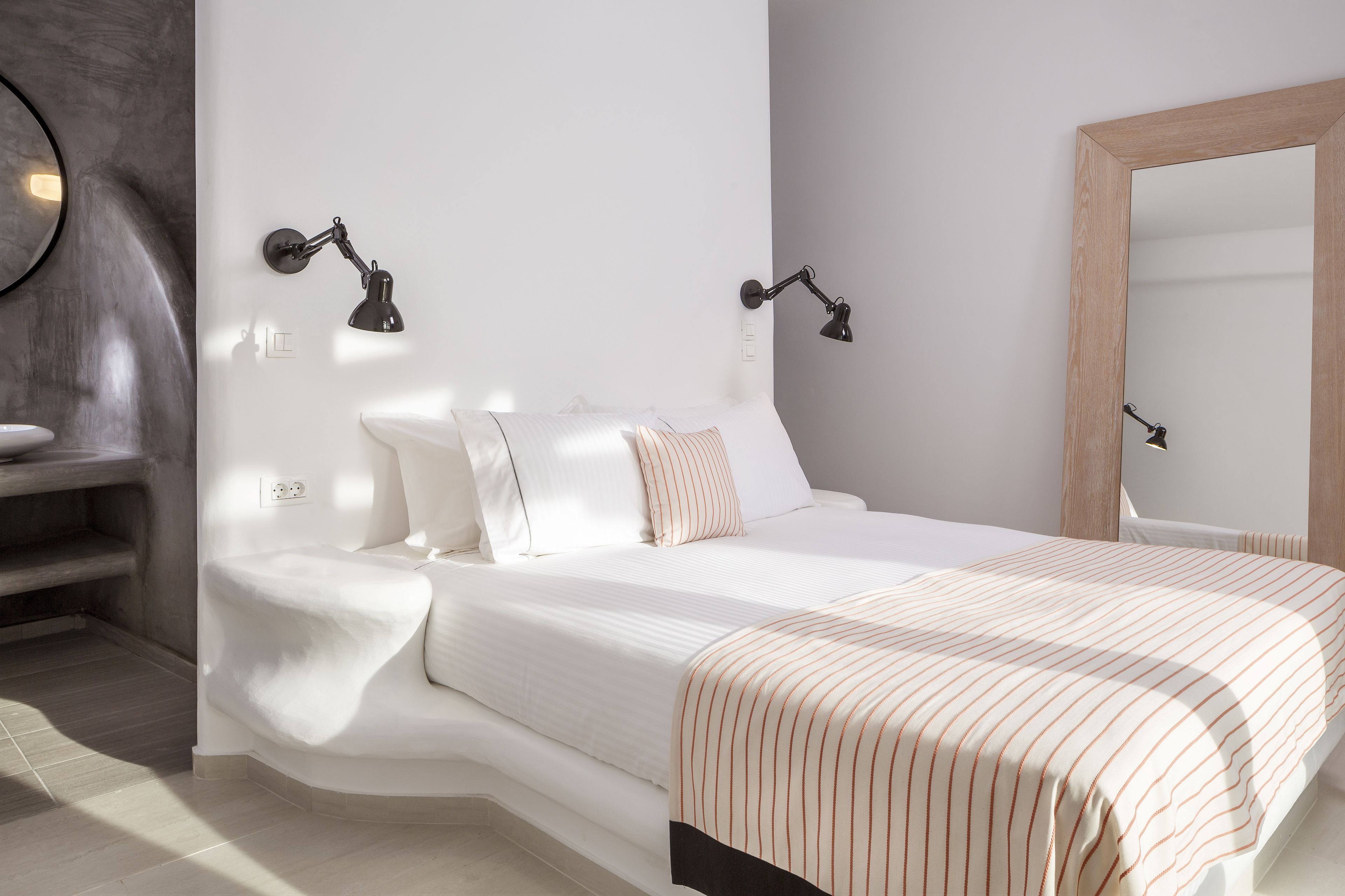 A neatly made bed with a striped blanket, two bedside lamps, and a large mirror on the wall.