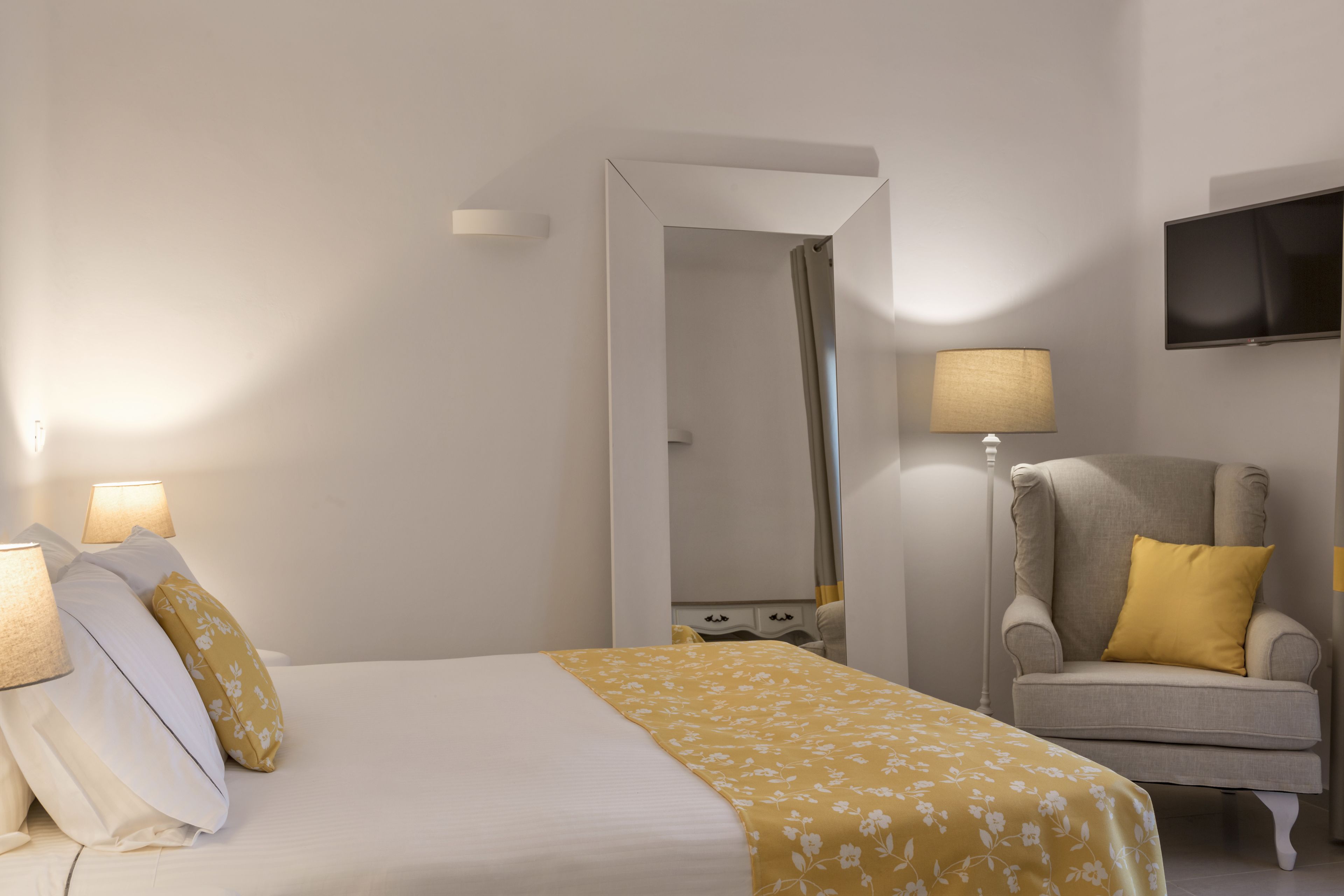 A hotel room with a bed, a chair, a TV, and a mirror.