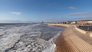 A beach with a wooden boardwalk, a lighthouse, and buildings along the shore. - Howarth House Apartments (Lytham St. Anne's)