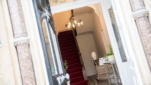 A grand staircase with a red carpet, a chandelier, and classical architectural details. - Howarth House Apartments (Lytham St. Anne's)