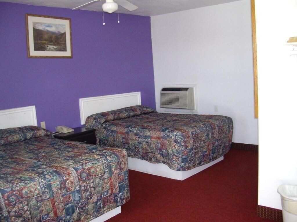 A room with two beds, a ceiling fan, an air conditioning unit, and a framed picture on the wall.