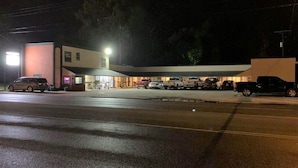 A building with a flat roof, a parking lot, and several vehicles parked in front. - Relax Inn Motel (Kountze)