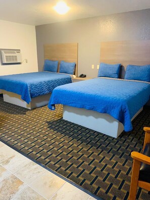 Two single beds with blue bedding, a wall-mounted air conditioner, and a patterned carpet.
