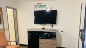 A hotel room with a television mounted on the wall, a minibar, a desk, and a chair. - Relax Inn Motel (Kountze)