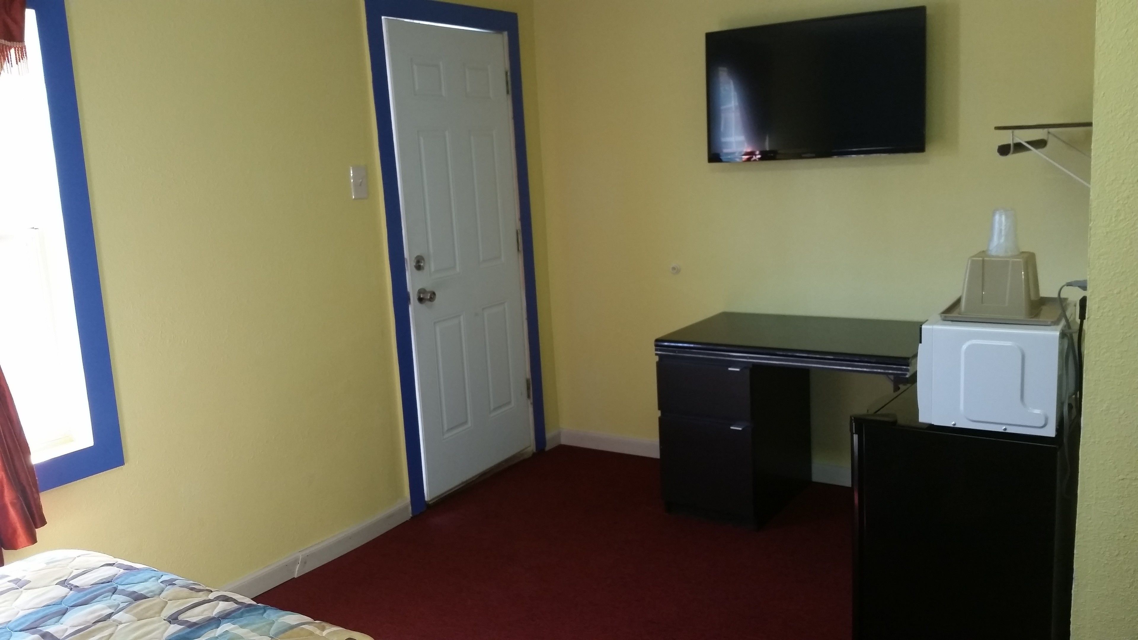 A small room with a bed, a desk, a chair, a television, and a microwave.