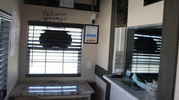 A reception area with a 'Welcome' sign, a window with blinds, a counter with a phone, and a 'No Refunds' sign. - Relax Inn Motel (Kountze)