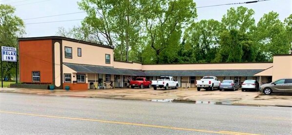 A motel with a single-story building, a covered parking area, and several vehicles parked.
