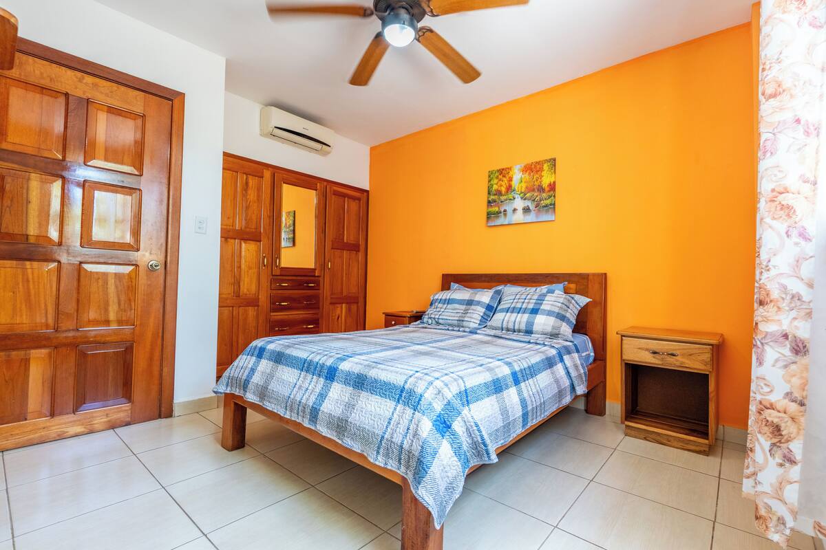 A bedroom with a bed, wooden wardrobe, nightstand, and a ceiling fan.