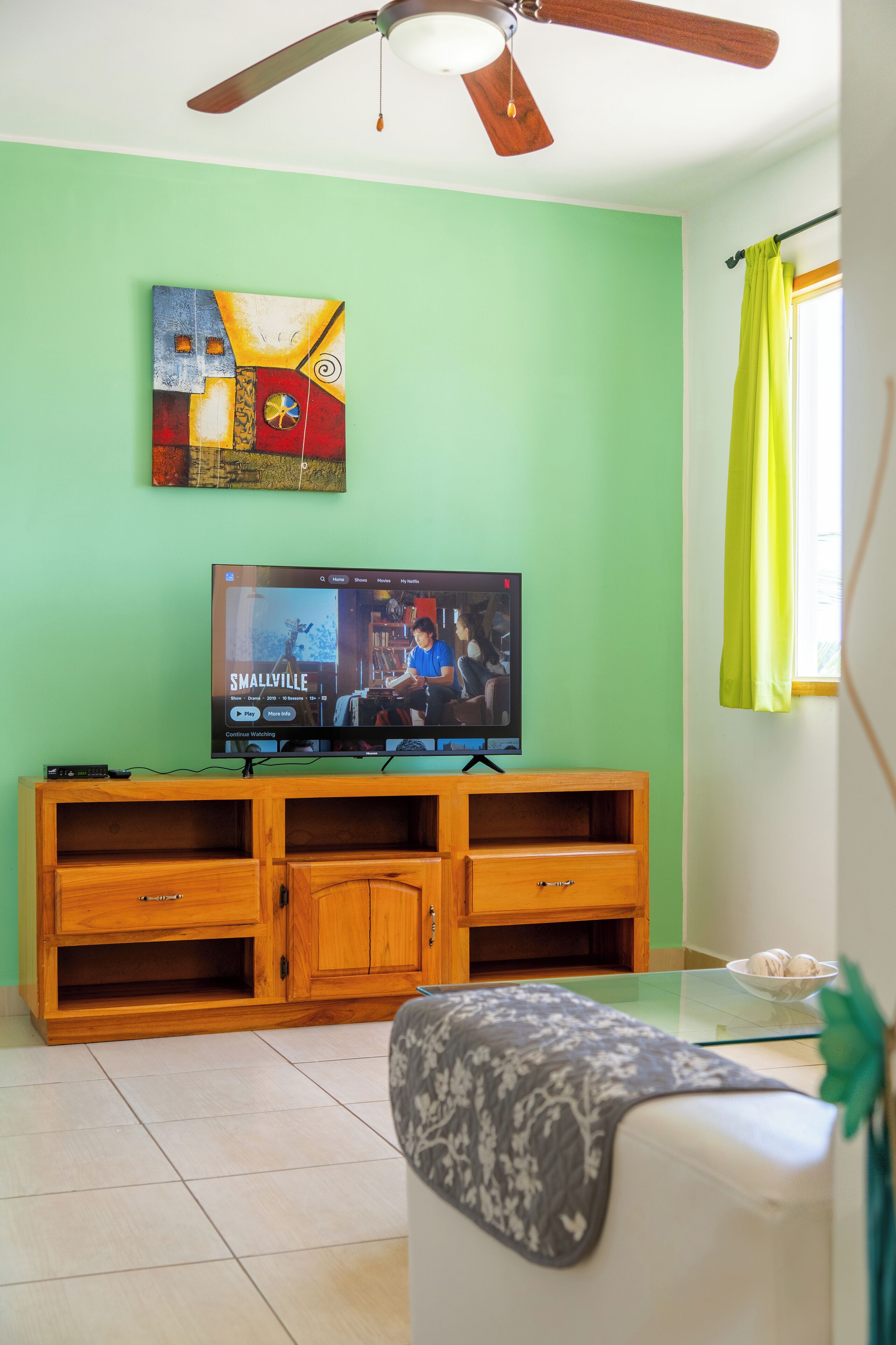 A living room with a television, wooden entertainment unit, and a ceiling fan.