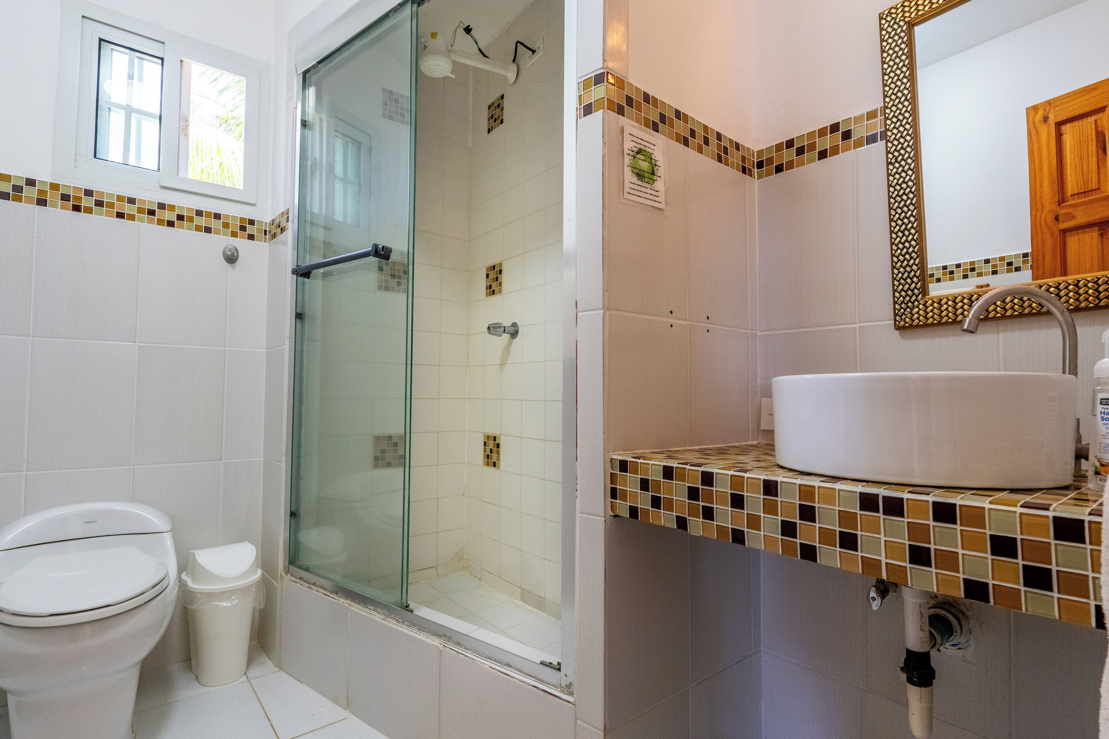 A bathroom with a toilet, a glass shower enclosure, a sink with a mirror, and tiled walls.
