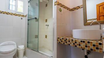 A bathroom with a toilet, a glass shower enclosure, a sink with a mirror, and tiled walls.