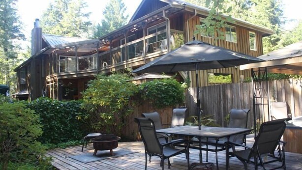 A wooden deck with a table and chairs, a fire pit, and a covered patio area. - Sea Star Beach Retreat (Tofino)