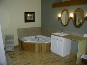 A bathroom with a wooden floor, a large bathtub, a sink, and two wall-mounted mirrors. - Sea Star Beach Retreat (Tofino)