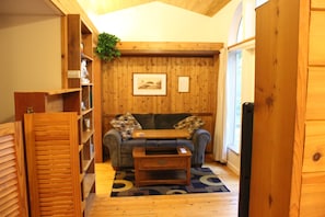 Ein gemütliches Zimmer mit Holzwänden, einer Couch, einem Couchtisch und einem Bücherregal.