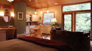 A cozy room with a bed, a desk, a chair, a dining table, and a window with a view of greenery. - Sea Star Beach Retreat (Tofino)