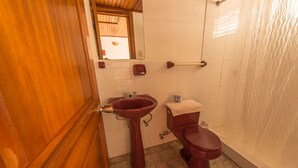 Un baño con puerta de madera, un lavamanos rojo, un inodoro y una cortina de ducha.