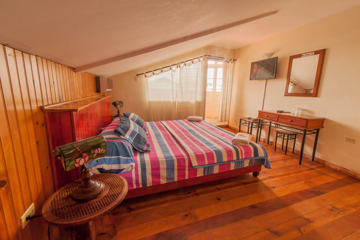 A bedroom with a bed, a desk, a chair, a mirror, and a window with curtains.