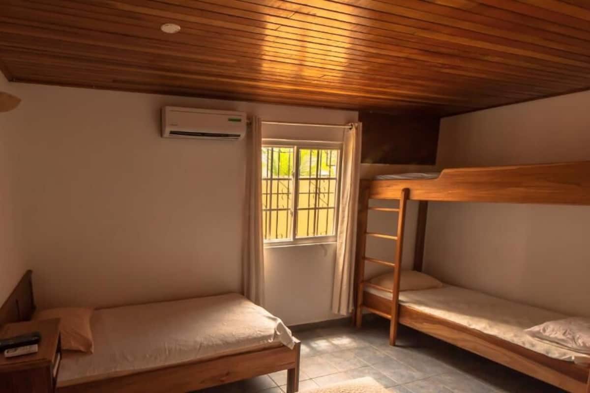 A small, cozy room with two bunk beds, a single bed, a wooden ceiling, and a window with bars.