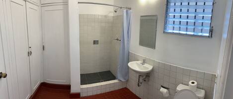 Baño con ducha, inodoro, lavabo y ventana con persianas.