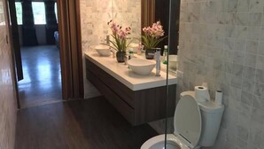 Une salle de bain moderne avec un grand miroir, un lavabo blanc et des toilettes. Deux plantes en pot sont posées sur le comptoir du lavabo.