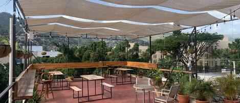 An outdoor patio with wooden benches and tables, potted plants, and a view of the cityscape.