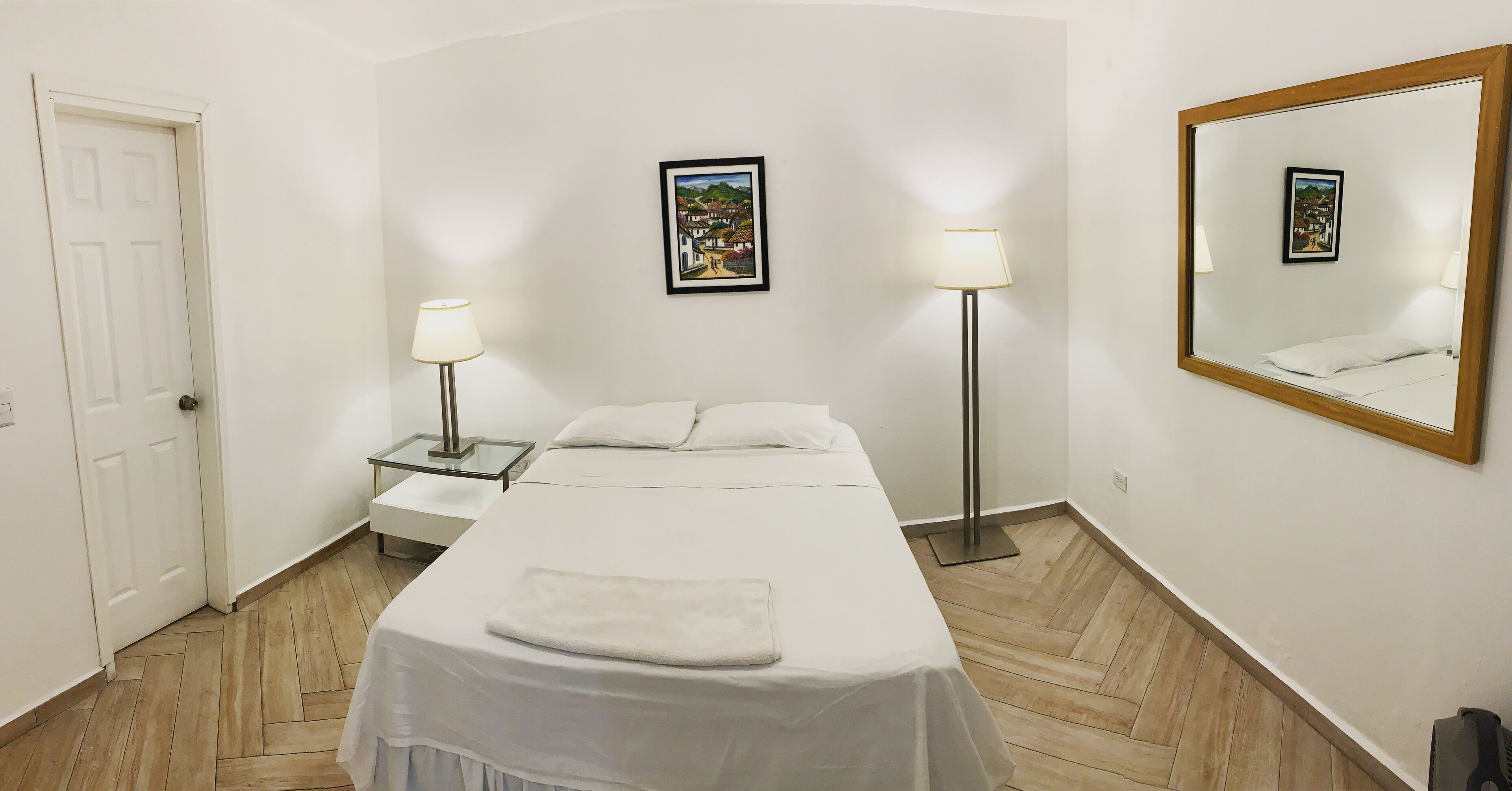 Une chambre d’hôtel avec un lit, deux lampes de chevet, une table de chevet, un miroir et une porte.