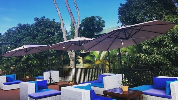 Espace extérieur aménagé avec des parasols, des meubles en osier blanc et des coussins bleus.