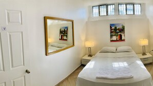 Une chambre à coucher avec un lit, deux tables de chevet avec des lampes, une plante en pot et un tableau au mur.