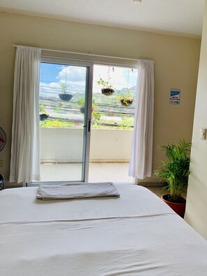 Et hotelværelse med en seng, en potteplante, et skilt for vaskeservice og udsigt til en balkon med kaskader af planter.