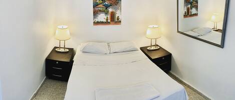 A neatly made bed with white linens, two bedside tables with lamps, and two wall-mounted paintings.