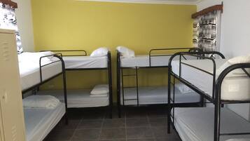 A dormitory room with bunk beds, a wardrobe, and a window with curtains.