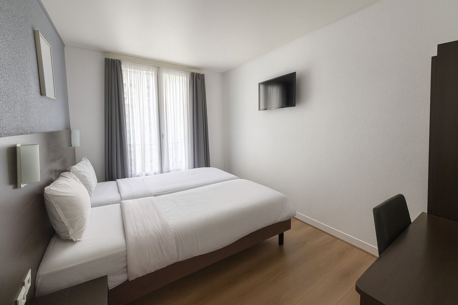 Una habitación de hotel moderna con una cama grande, un televisor de pantalla plana en la pared y un escritorio de madera.