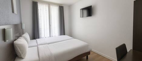 Una habitación de hotel moderna con una cama grande, un televisor de pantalla plana en la pared y un escritorio de madera.