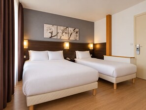 A hotel room with two beds, a wooden floor, a painting on the wall, and a door with a lock. - Hôtel Arc Paris Porte d’Orléans  (Montrouge)