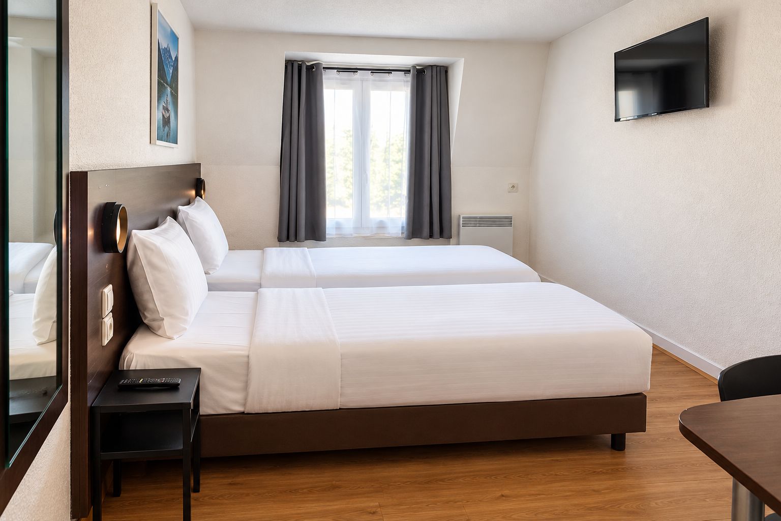 Ein Hotelzimmer mit zwei Betten, einem Flachbildfernseher, einem Schreibtisch und einem fensterbelaubten Fenster.