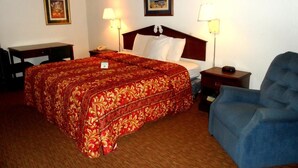 A hotel room with a large bed, a desk, two bedside lamps, a chair, and two framed pictures on the walls. - Budgetel Inn NASA (Houston)