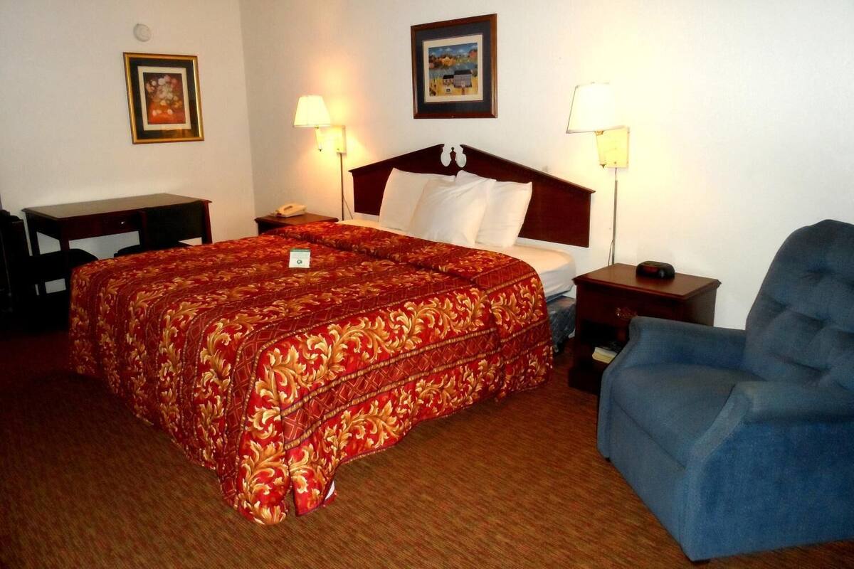A hotel room with a large bed, a desk, two bedside lamps, a chair, and two framed pictures on the walls.